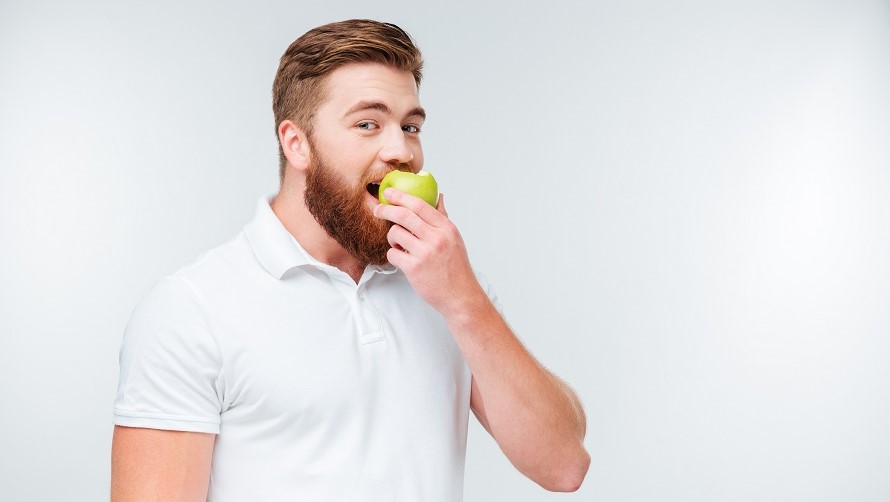 Junger Mann beisst in Apfel Junger Mann mit Bart beisst in einen grünen Apfel